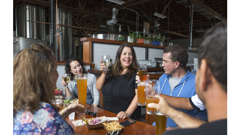 Five cheerful middle-aged adults toasting drinks during happy hour in a microbrewery.