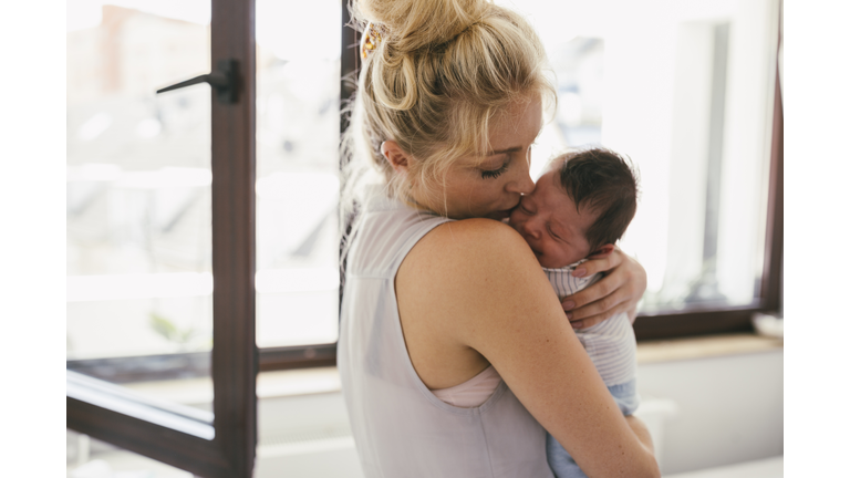 Mother holding her crying baby close to her shoulder at home