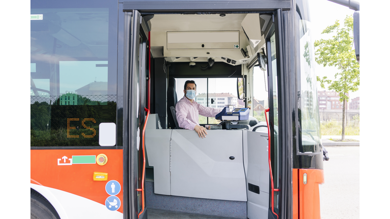 Mature bus driver wearing protective mask waiting at bus station, Spain