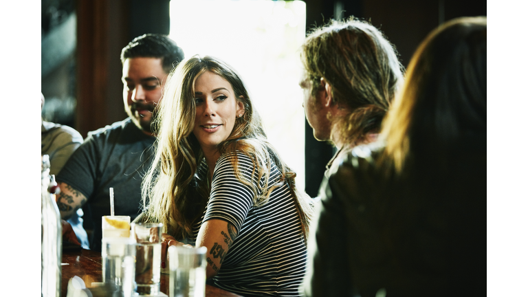 Smiling woman hanging out with friend while having drinks in bar