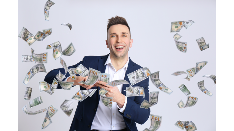 Happy young man with money on light background