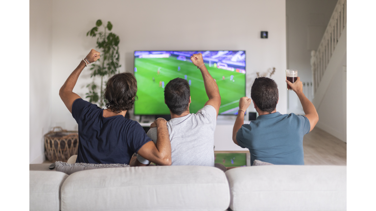 Three friends watching a soccer game at home drinking beer