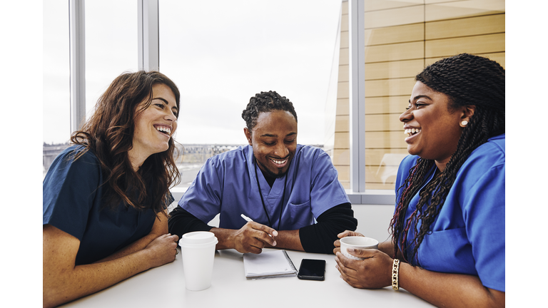 Cheerful male and female nurses talking at table in hospital