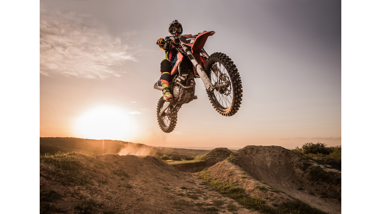 Motocross rider performing high jump at sunset.