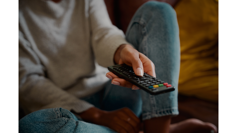 Closeup of young female hand holding remote control and changing channel at home watching television alone