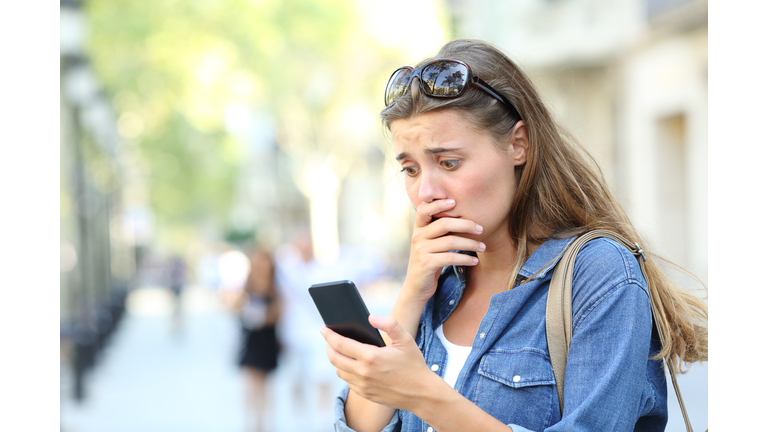 Worried girl checking smart phone in the street