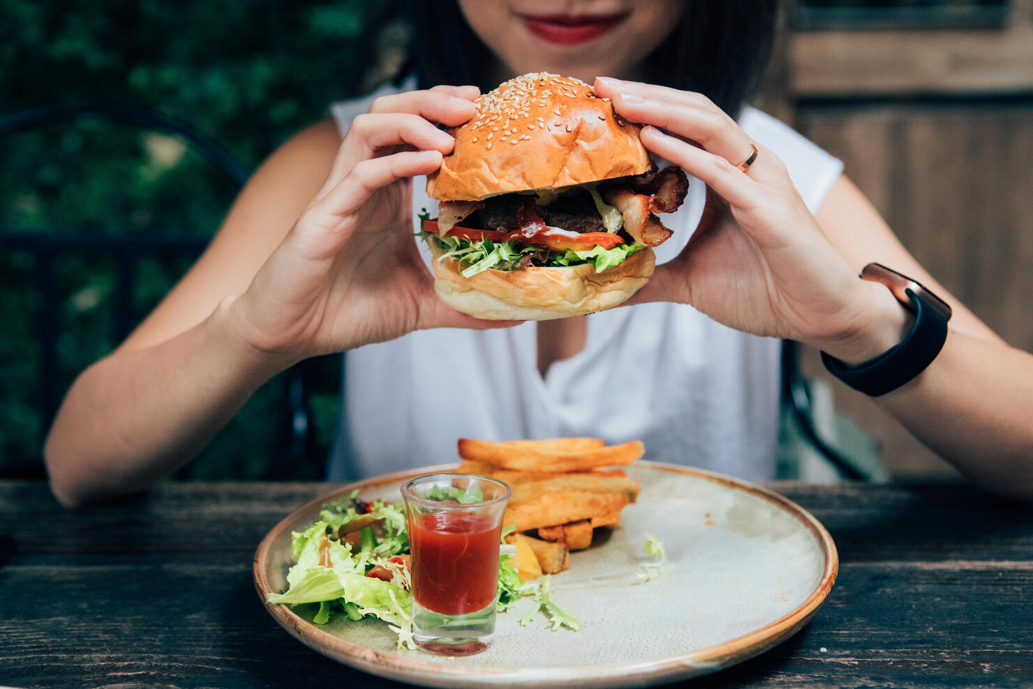 Young Woman Eating Burger At Restaurant With Outdoor Seating