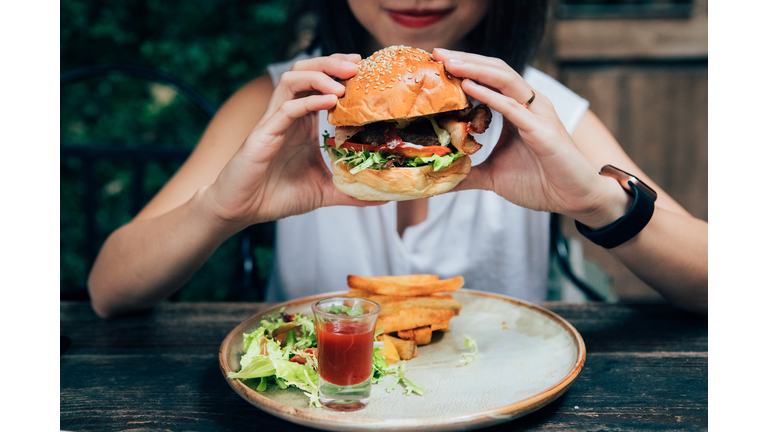 Young Woman Eating Burger At Restaurant With Outdoor Seating