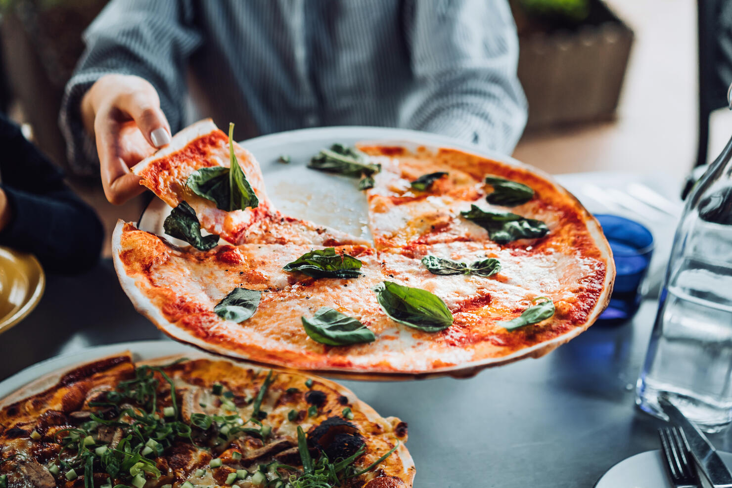 Close up of young Asian woman getting a slice of freshly made pizza. Enjoying her meal in an outdoor restaurant. Italian cuisine and culture. Eating out lifestyle