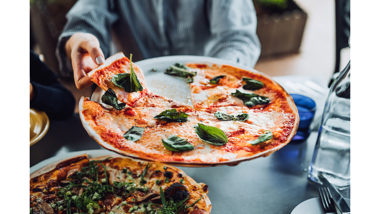 Close up of young Asian woman getting a slice of freshly made pizza. Enjoying her meal in an outdoor restaurant. Italian cuisine and culture. Eating out lifestyle