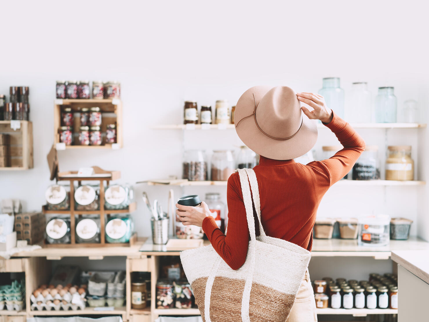 Minimalist vegan style girl with wicker bag and reusable glass coffee cup on background of interior of zero waste shop.