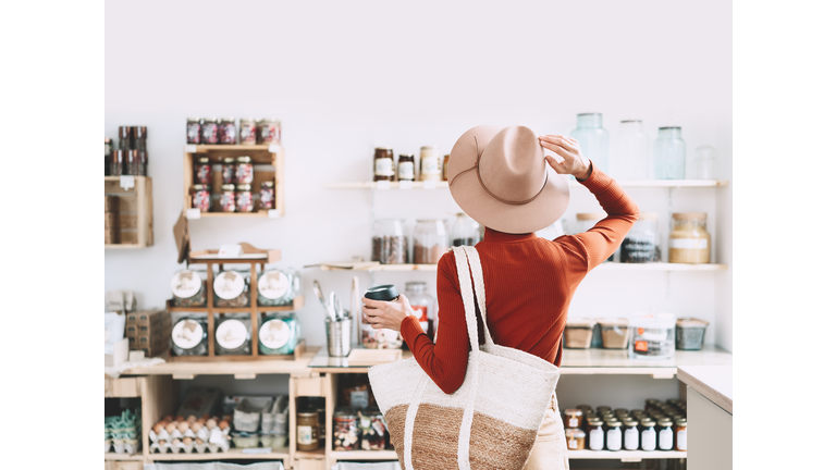 Minimalist vegan style girl with wicker bag and reusable glass coffee cup on background of interior of zero waste shop.