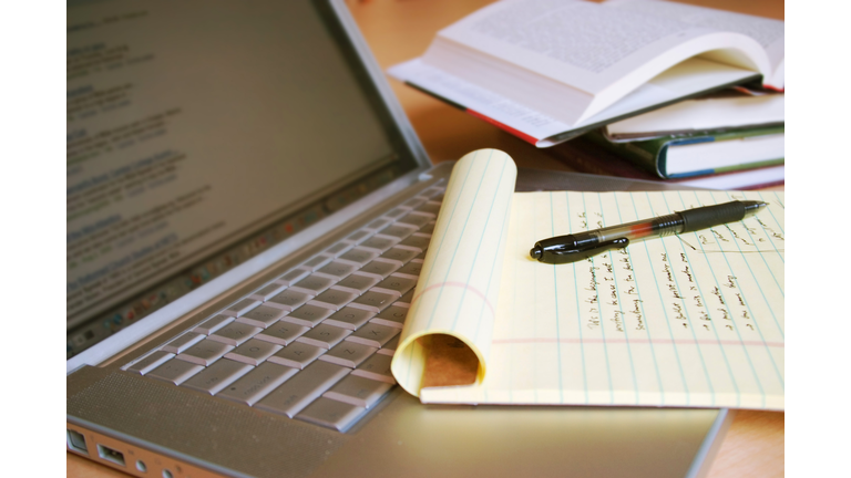 Laptop computer with books, pen and yellow legal pad