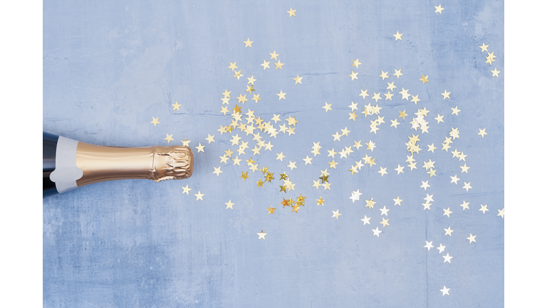 Champagne bottle with confetti stars on blue background. Holiday concept. Flat lay style. Copy space, top view.
