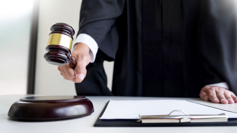 Midsection Of Judge Holding Gavel At Table In Courthouse