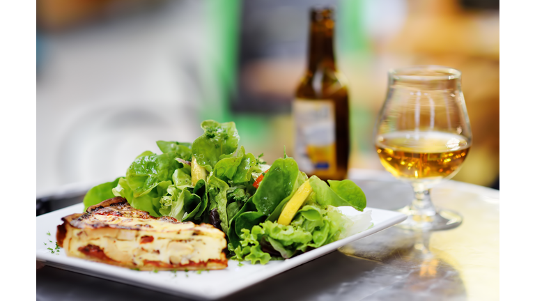 Traditional French food: quiche lorraine and fresh salad leaves with glass of beer on background