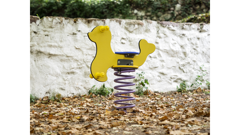 Rocking horse of wood with form of horse in a park outdoors in autumn with dry leaves on the ground.