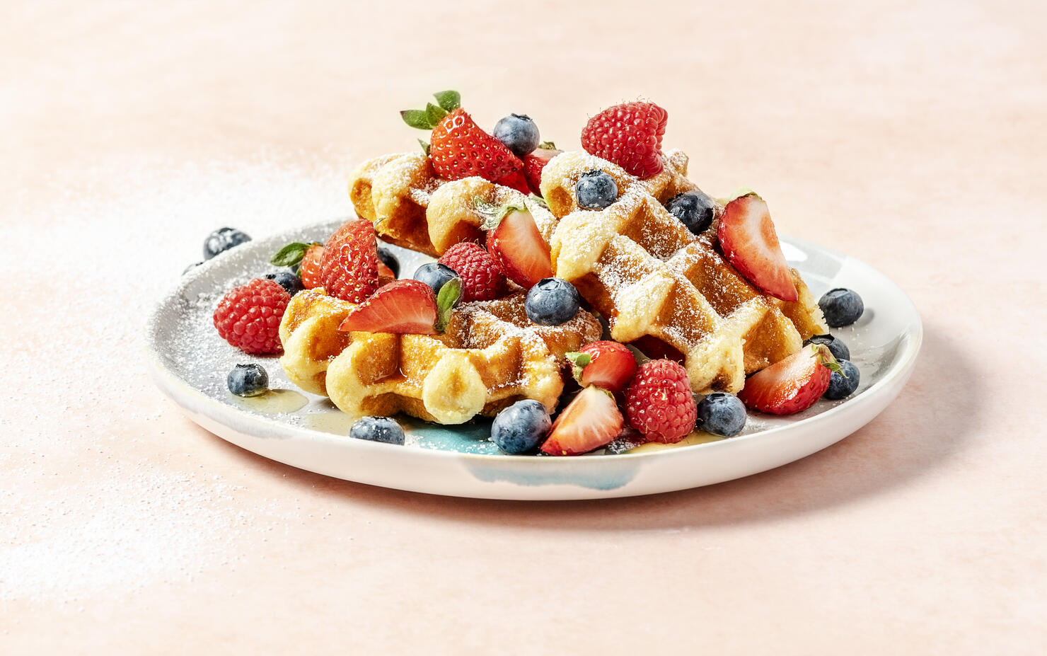 A plate of waffles with berries on peach background