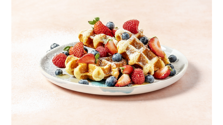 A plate of waffles with berries on peach background