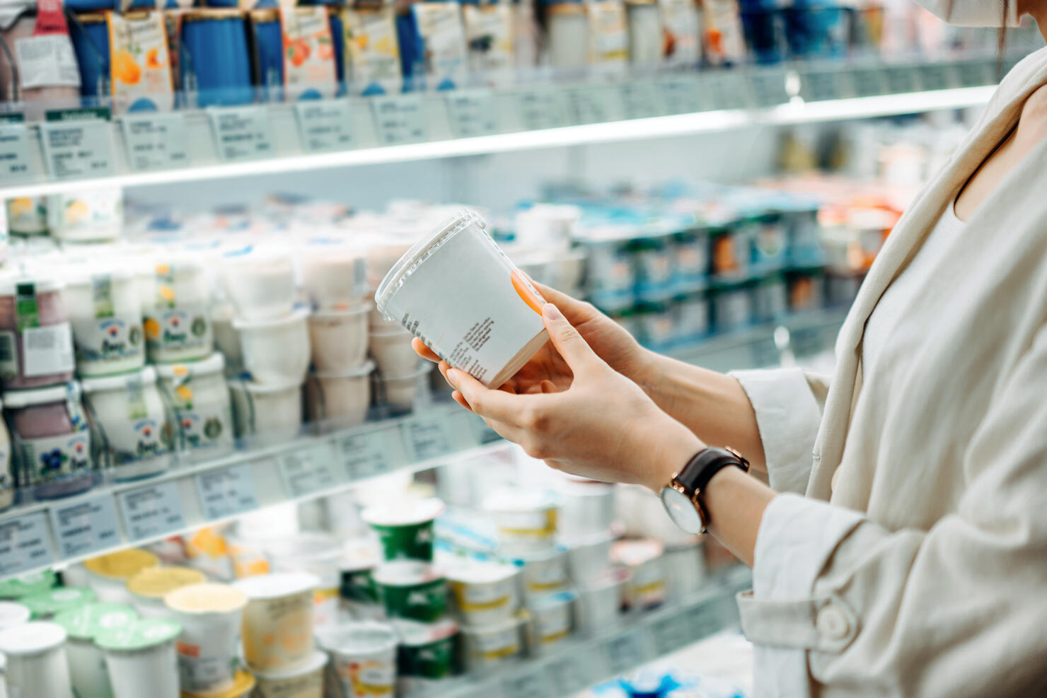 Cropped shot of young Asian woman shopping in the dairy section of a supermarket. She is reading the nutrition label on a container of fresh organic healthy natural yoghurt