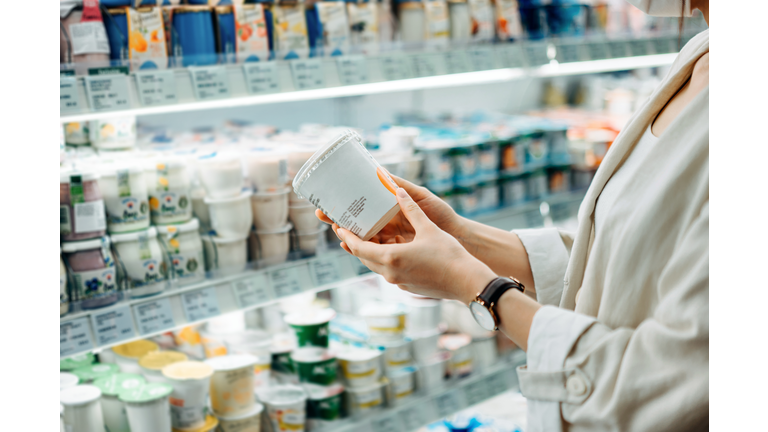 Cropped shot of young Asian woman shopping in the dairy section of a supermarket. She is reading the nutrition label on a container of fresh organic healthy natural yoghurt