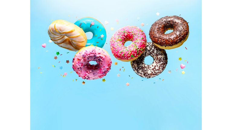 Flying delicious donuts with sprinkel on blue background with copy space