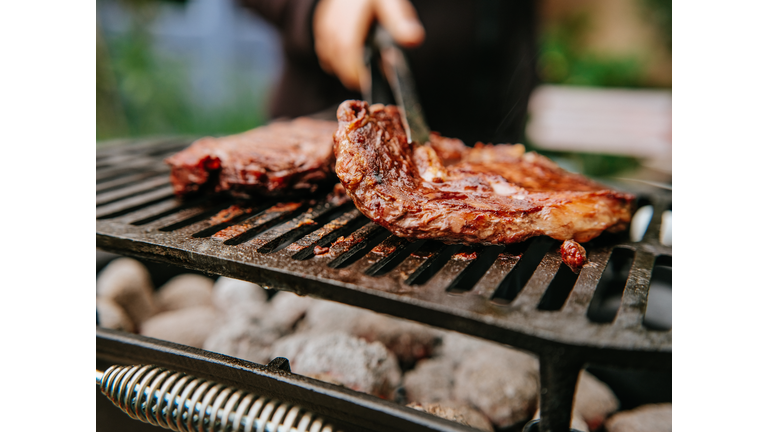 Woman doing BBQ Steaks on a flame grill.