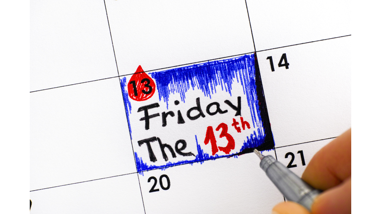 Woman fingers with pen writing reminder Friday The 13th in calendar.