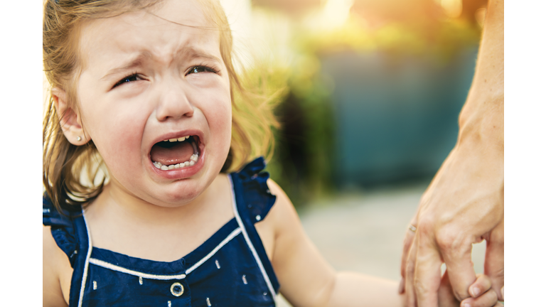 Close up portrait of crying little toddler girl with outdoors background. Child