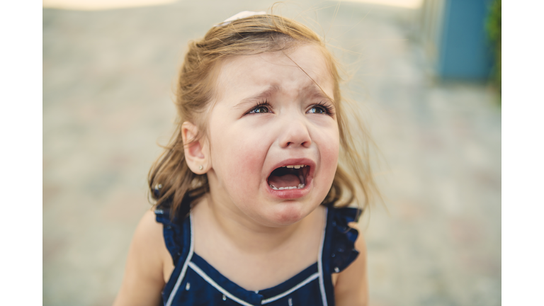 Close up portrait of crying little toddler girl with outdoors background. Child