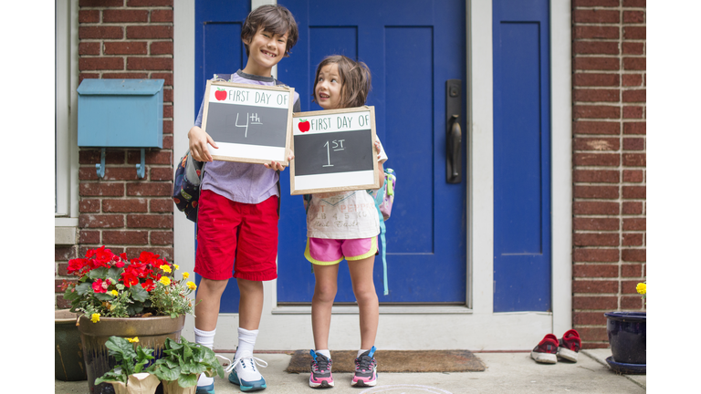 Two siblings stand together on stoop holding First Day of School signs