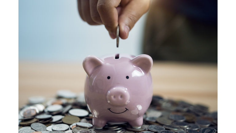 Person Putting Coin In Piggy Bank At Table