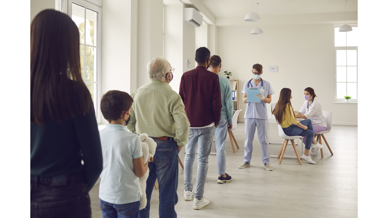 Diverse people lining up waiting for their turn to get shots in modern vaccination center