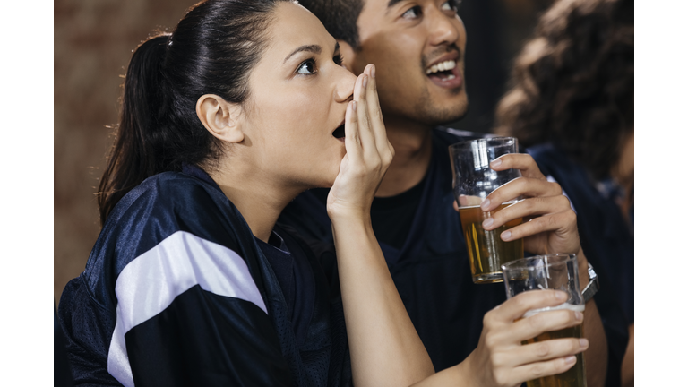 Woman covering mouth while watching soccer match with friend in bar