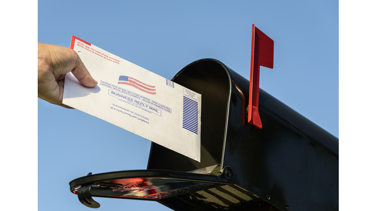 Woman's hand placing a 2020 mail-in election ballot in a rural mailbox