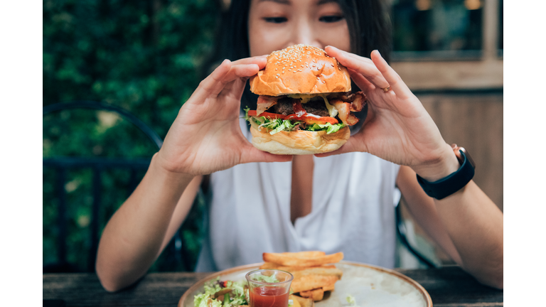 Young Woman Eating Burger At Restaurant With Outdoor Seating