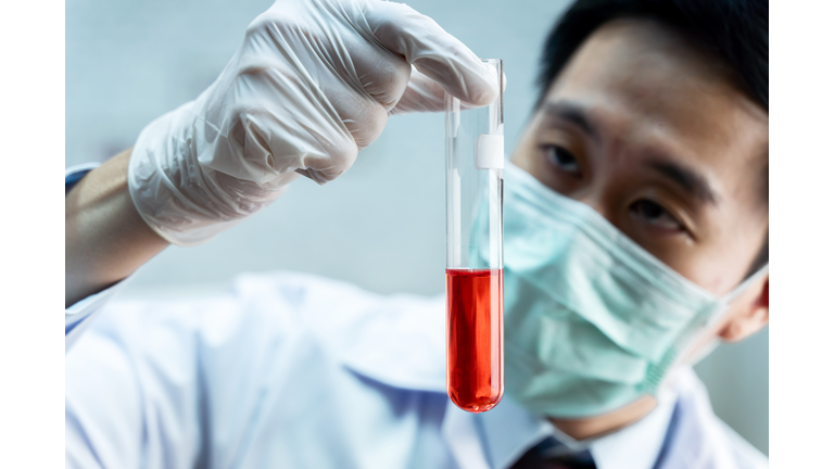 Close-up of Asian male scientist in white uniform holding laboratory flask with red chemical solution. Chemistry, Science, Biological, Toxicology, Research and Development concept