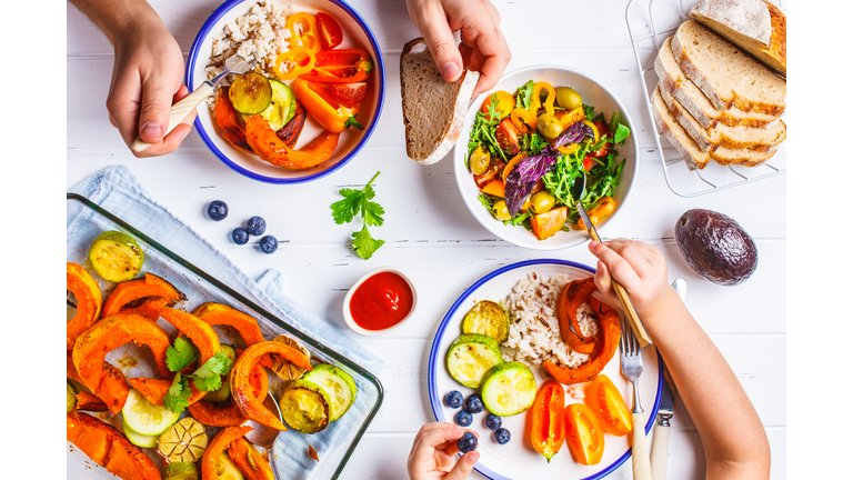 Family eating a healthy vegetarian food. Vegan lunch table top view, plant based diet. Baked vegetables, fresh salad, berries, bread on a white background.