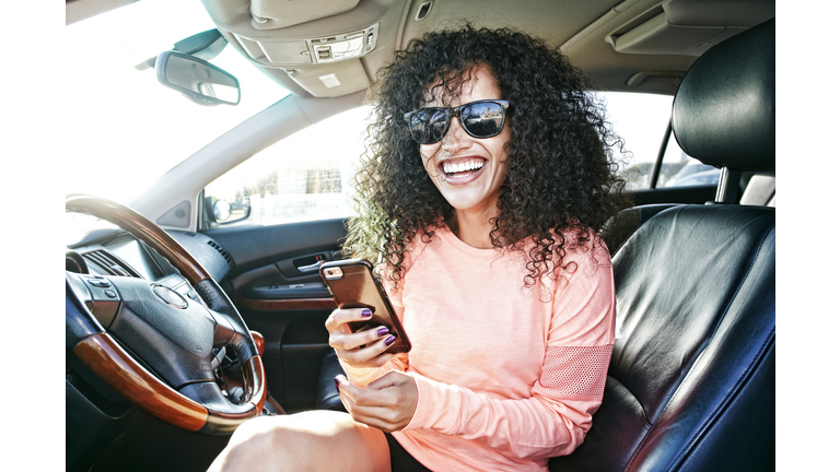 Laughing Hispanic woman in car holding texting on cell phone