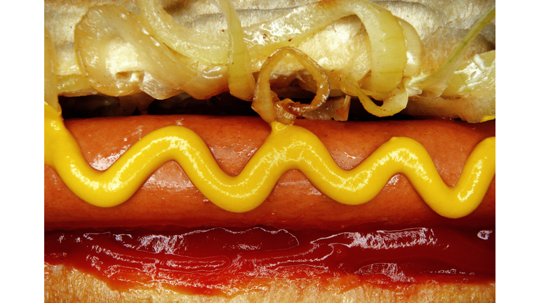 Hotdog with mustard, tomato ketchup and onions, close-up