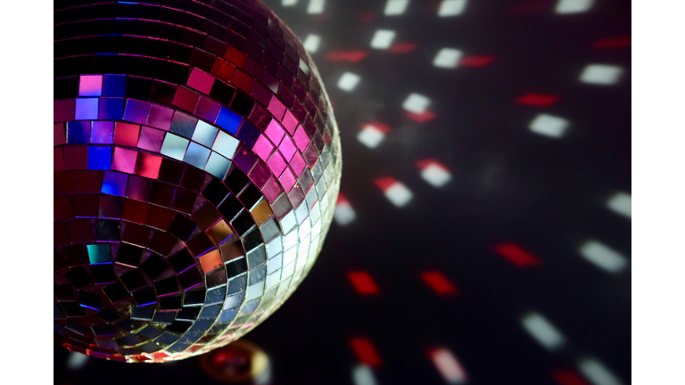 close up part of colorful disco ball light hanging on ceiling. red and white lights on dark background