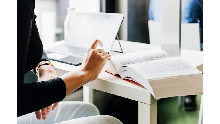 University Student Looking Through Large Textbook While Working