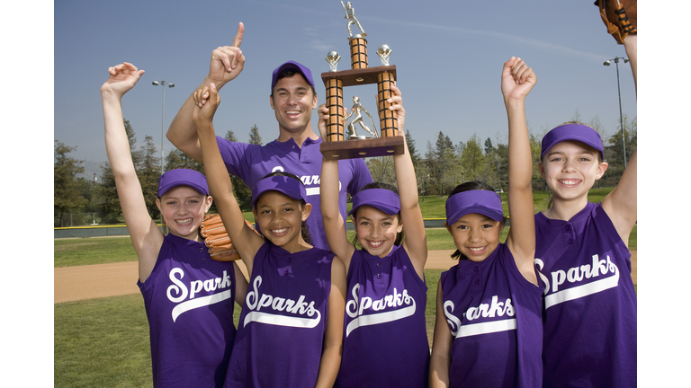 Portrait of little league softball team with coach holding trophy