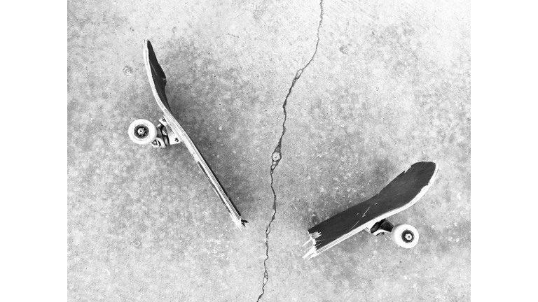 Broken skateboard on a sidewalk crack.