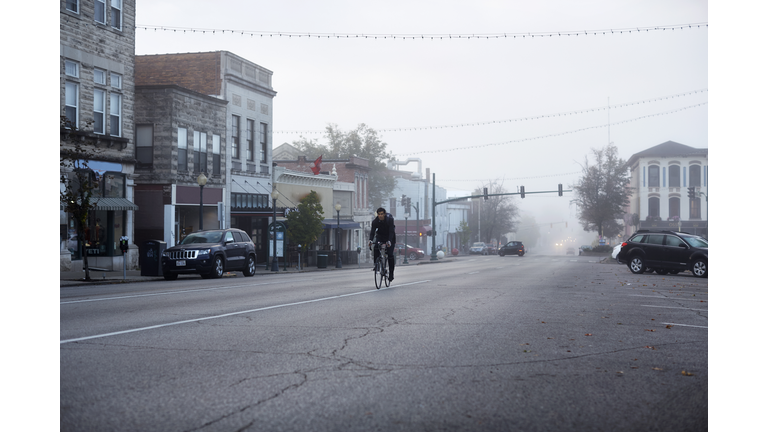 Commuter riding bike rides towards camera on small town square