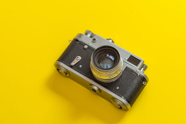 Retro, vintage film camera on a yellow colorful fashionable modern background. Camera lens with reflections. Film camera
