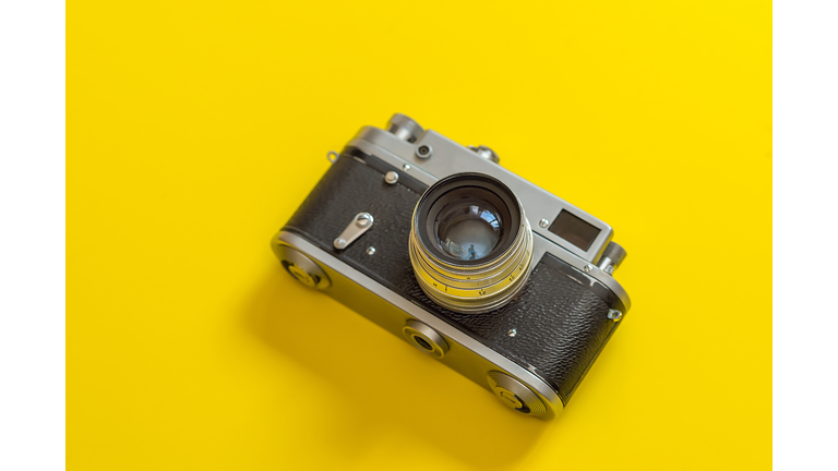Retro, vintage film camera on a yellow colorful fashionable modern background. Camera lens with reflections. Film camera