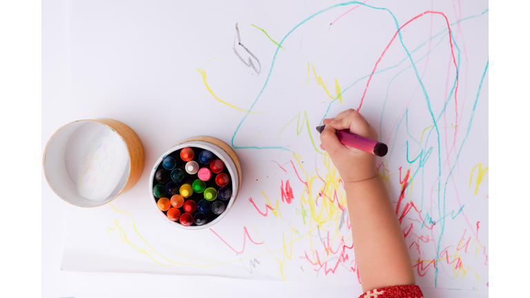 A hand of baby drawing lines and shapes with colorful crayons.