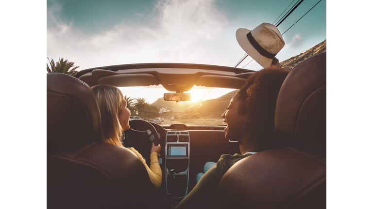 Happy girls doing road trip in tropical city - Travel people having fun driving in trendy convertible car discovering new places - Friendship and youth girlfriends vacation lifestyle concept