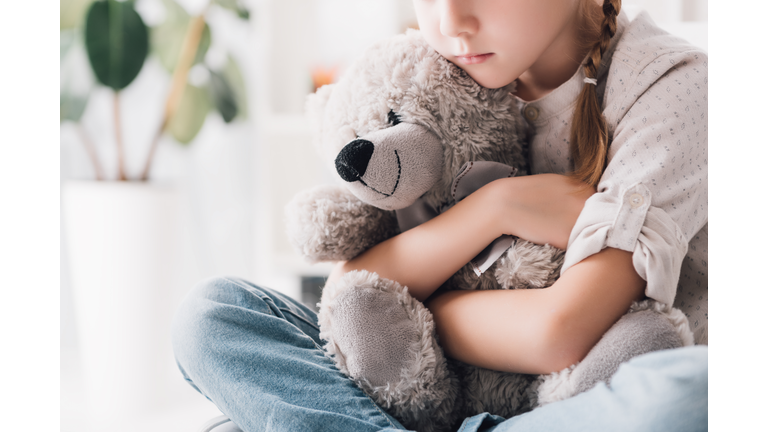 cropped shot of depressed little child embracing her teddy bear